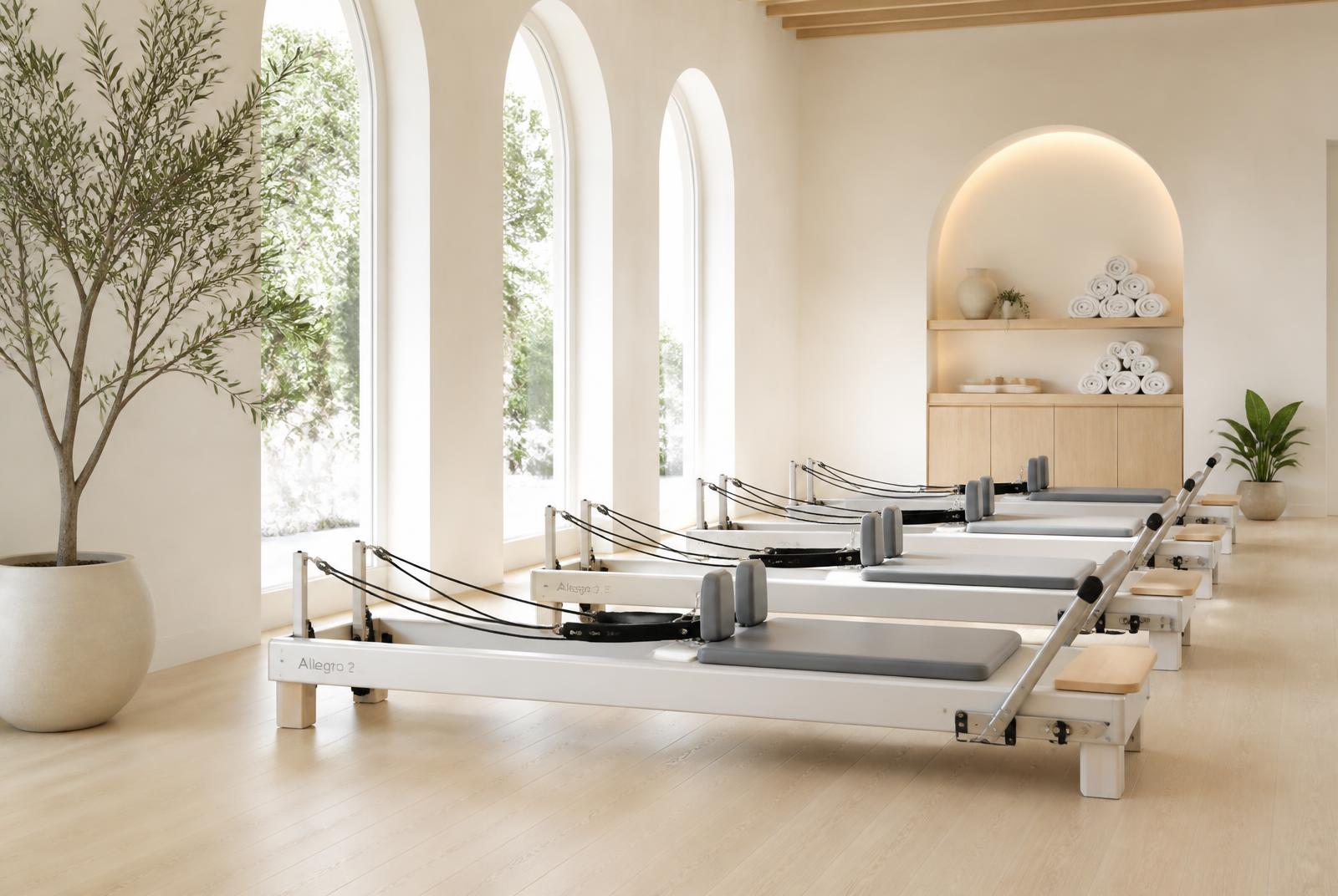 Row of white and wood Balanced Body Allegro 2 reformers in a sunlit ivory studio